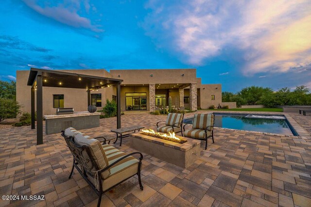 pool at dusk with an outdoor fire pit, exterior kitchen, and a patio