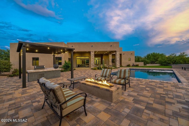 pool at dusk featuring an outdoor pool, area for grilling, a ceiling fan, and a patio area