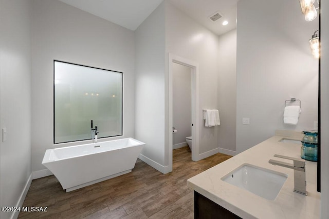 full bathroom featuring baseboards, toilet, a freestanding tub, wood finished floors, and a sink