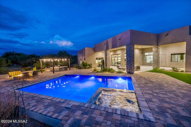 pool at night with an in ground hot tub and a patio area