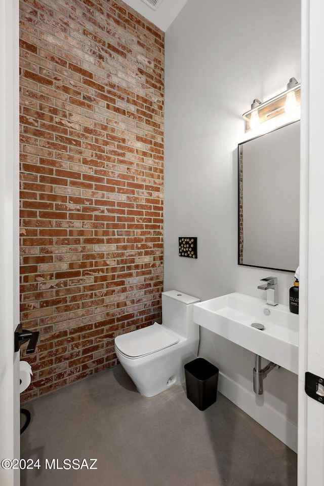 bathroom with concrete floors, brick wall, toilet, and sink