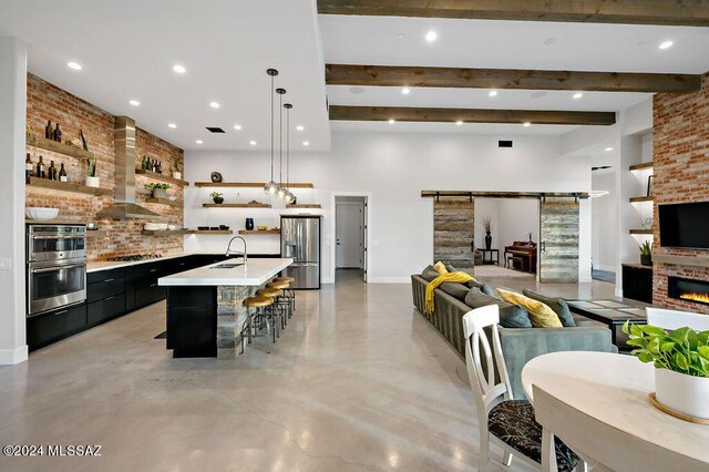 kitchen featuring a kitchen island with sink, stainless steel appliances, sink, wall chimney exhaust hood, and a barn door