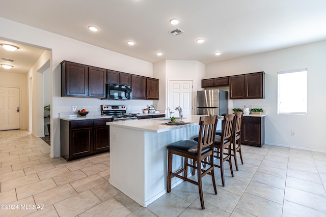 kitchen with a kitchen island with sink, sink, a breakfast bar, appliances with stainless steel finishes, and dark brown cabinetry