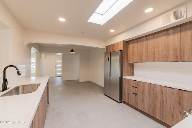 kitchen with freestanding refrigerator, brown cabinets, a sink, and modern cabinets