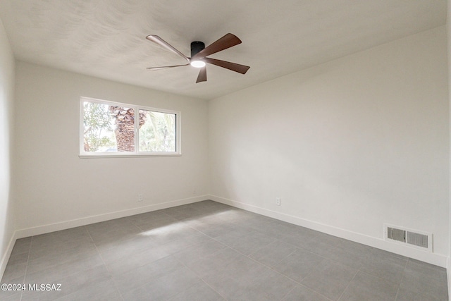 tiled empty room featuring baseboards, visible vents, and a ceiling fan