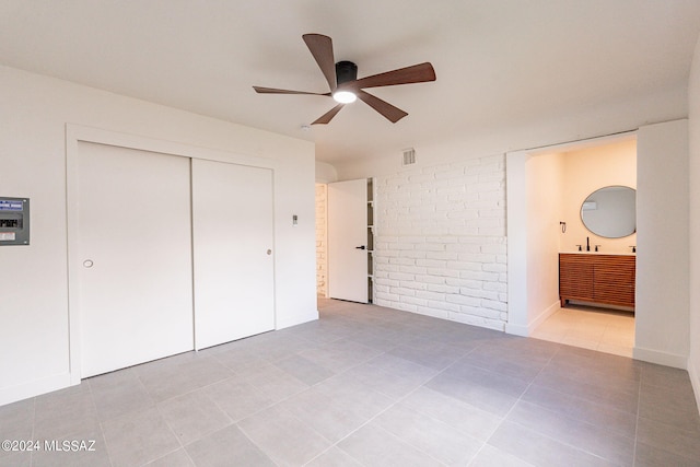 unfurnished bedroom featuring visible vents, connected bathroom, brick wall, tile patterned floors, and a closet