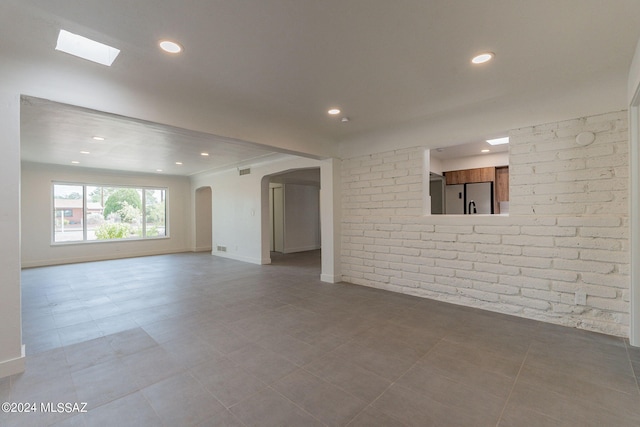 spare room featuring arched walkways, brick wall, baseboards, and recessed lighting