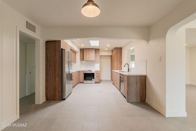 kitchen featuring a sink, light countertops, appliances with stainless steel finishes, brown cabinetry, and modern cabinets