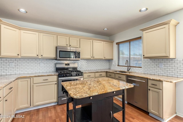 kitchen with a sink, stainless steel appliances, cream cabinetry, tasteful backsplash, and light wood-style flooring