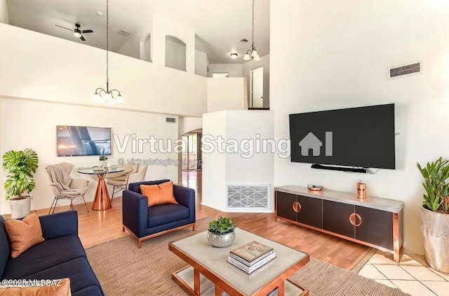 living room with visible vents, light wood-type flooring, high vaulted ceiling, and ceiling fan with notable chandelier