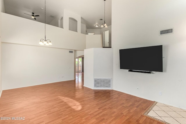 unfurnished living room with visible vents, ceiling fan with notable chandelier, light wood finished floors, and a towering ceiling