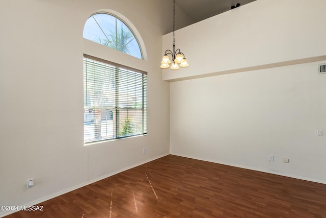 unfurnished room with wood finished floors, a chandelier, baseboards, visible vents, and a high ceiling