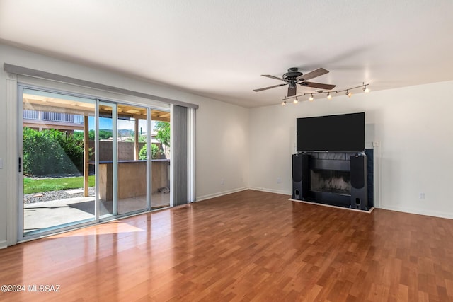 unfurnished living room with track lighting, a wealth of natural light, ceiling fan, and a fireplace with raised hearth