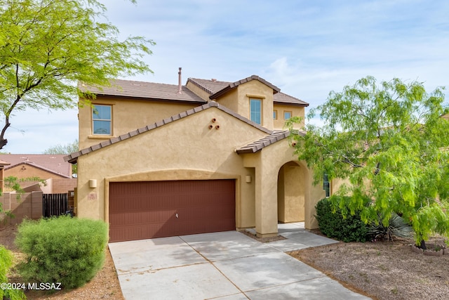 mediterranean / spanish home with a garage, fence, concrete driveway, a tiled roof, and stucco siding