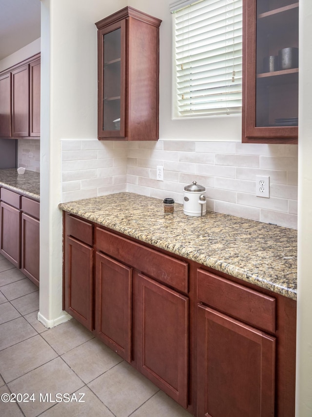 kitchen featuring light stone countertops, light tile patterned floors, tasteful backsplash, and glass insert cabinets