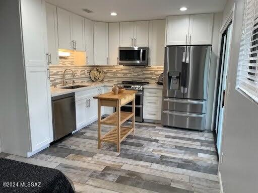 kitchen featuring light hardwood / wood-style flooring, stainless steel appliances, backsplash, sink, and white cabinetry