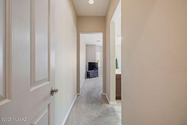 corridor featuring baseboards and light carpet