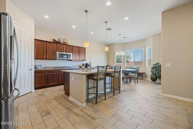 kitchen featuring appliances with stainless steel finishes, a breakfast bar, an island with sink, and wood tiled floor