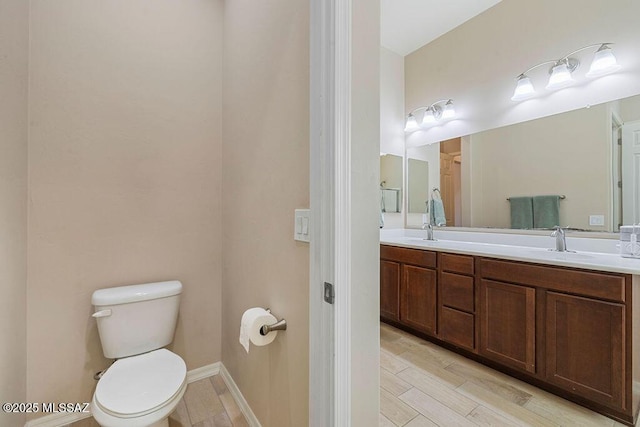 full bathroom with double vanity, wood finished floors, toilet, baseboards, and a sink