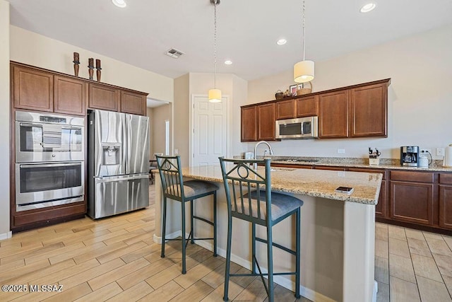 kitchen with wood finish floors, appliances with stainless steel finishes, visible vents, and light stone countertops