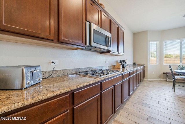 kitchen with appliances with stainless steel finishes, a toaster, baseboards, light stone counters, and light wood finished floors