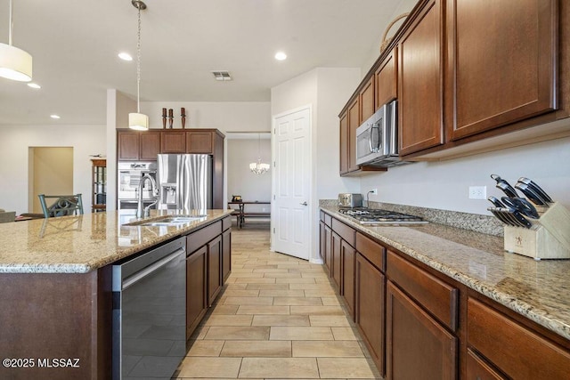 kitchen with visible vents, light stone countertops, a sink, stainless steel appliances, and an island with sink