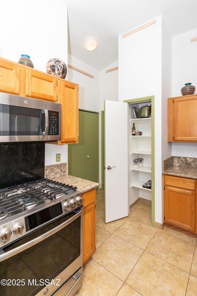 kitchen with light tile patterned flooring, appliances with stainless steel finishes, vaulted ceiling, and light stone counters