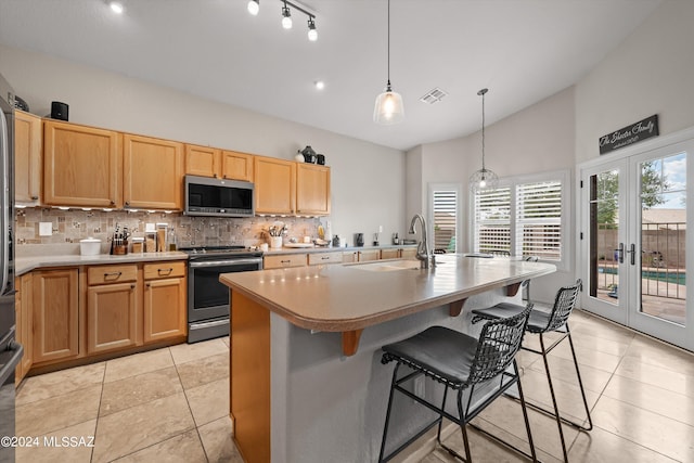 kitchen featuring appliances with stainless steel finishes, french doors, backsplash, hanging light fixtures, and a kitchen island with sink