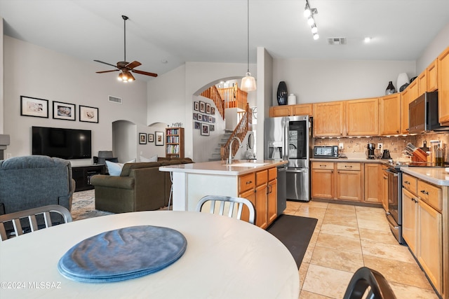 kitchen with a center island with sink, stainless steel appliances, tasteful backsplash, decorative light fixtures, and sink