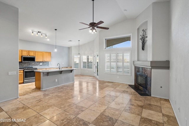 kitchen featuring appliances with stainless steel finishes, an island with sink, decorative backsplash, vaulted ceiling, and ceiling fan