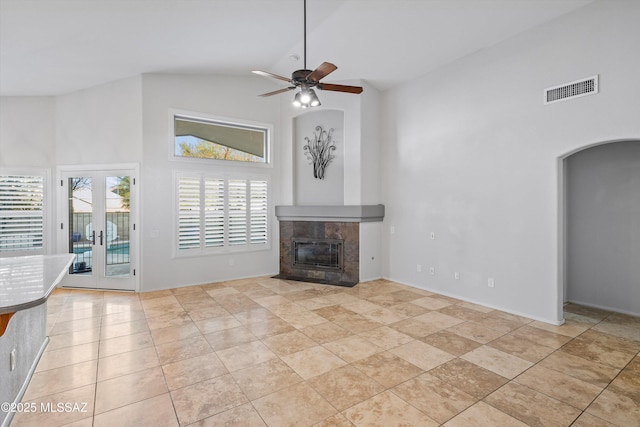 unfurnished living room with ceiling fan, a tile fireplace, high vaulted ceiling, light tile patterned floors, and french doors