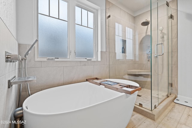 bathroom with wood-type flooring, tile walls, and separate shower and tub