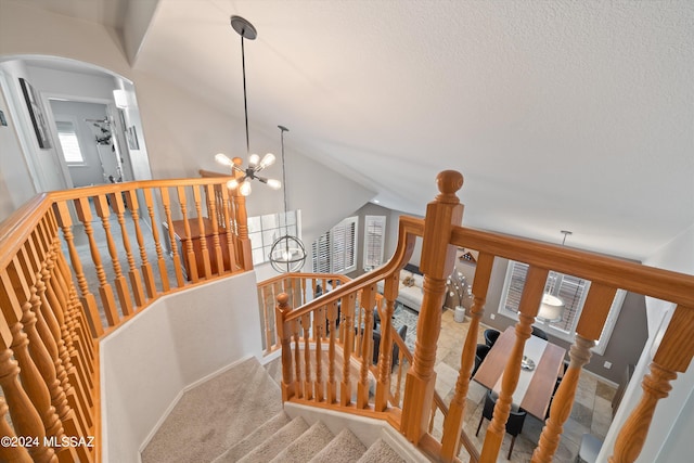 stairway with vaulted ceiling, a notable chandelier, and carpet flooring