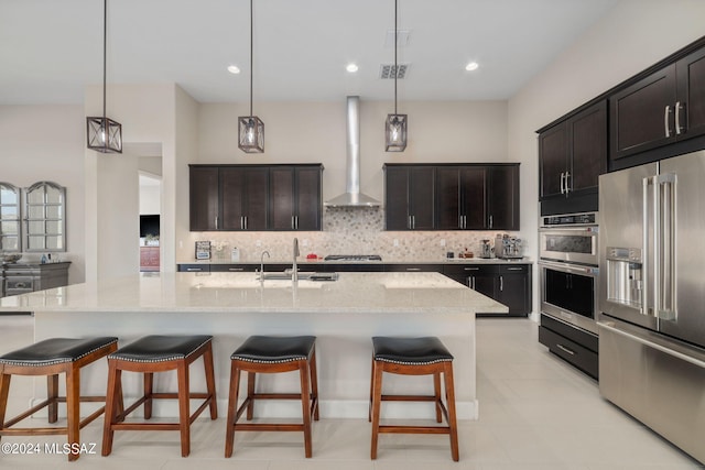 kitchen featuring pendant lighting, an island with sink, appliances with stainless steel finishes, and wall chimney exhaust hood