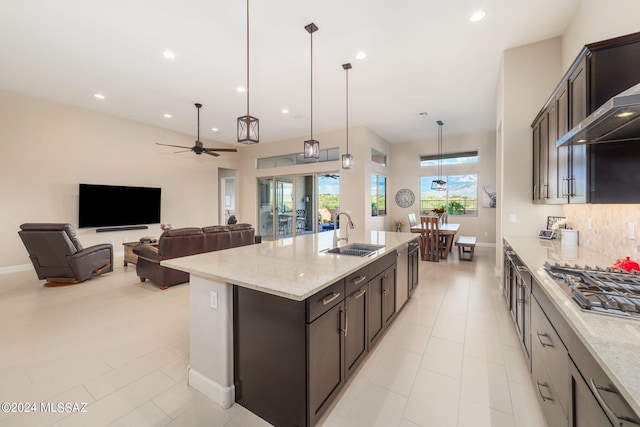 kitchen with pendant lighting, a kitchen island with sink, sink, light stone countertops, and ceiling fan