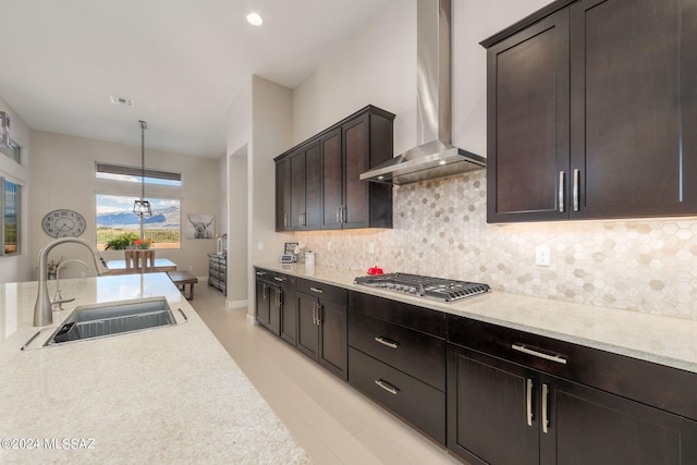 kitchen with hanging light fixtures, sink, wall chimney range hood, stainless steel gas stovetop, and decorative backsplash