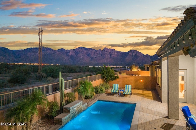 pool at dusk featuring pool water feature, a mountain view, and a patio area