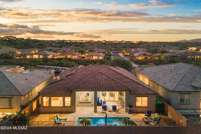 back house at dusk with a fenced in pool and a patio