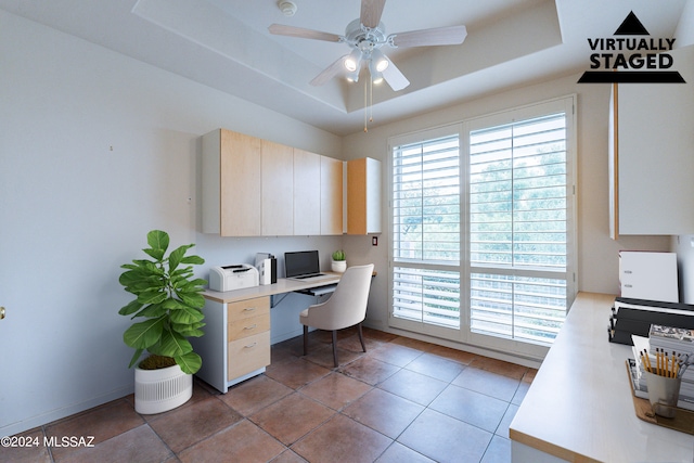 tiled office space with a raised ceiling and ceiling fan