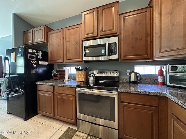 kitchen featuring light tile patterned floors, appliances with stainless steel finishes, brown cabinetry, and dark stone countertops