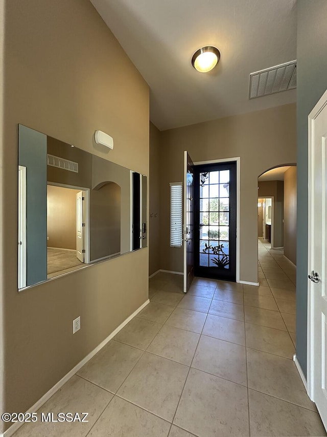 entrance foyer featuring light tile patterned floors, arched walkways, visible vents, and baseboards