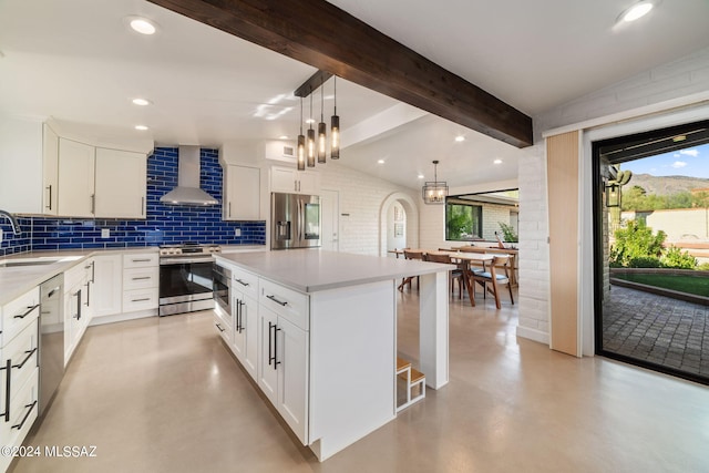 kitchen with decorative light fixtures, wall chimney range hood, a kitchen island, stainless steel appliances, and white cabinets