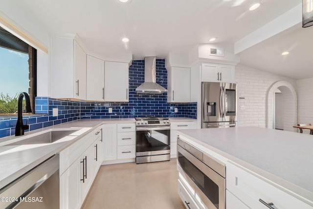 kitchen with white cabinets, appliances with stainless steel finishes, wall chimney exhaust hood, decorative backsplash, and sink