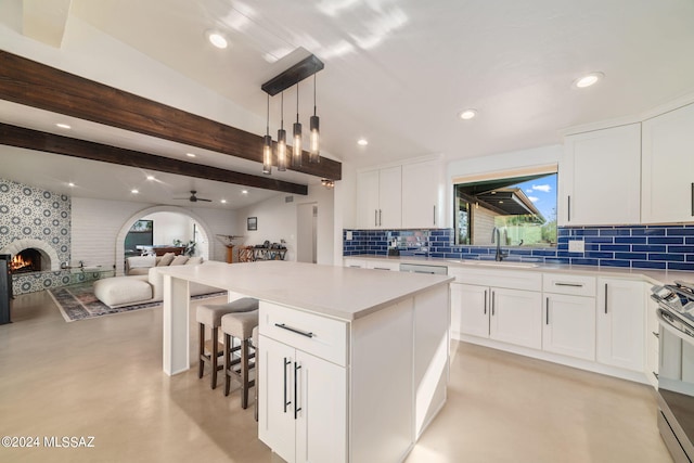 kitchen with decorative light fixtures, a large fireplace, white cabinetry, and stainless steel stove