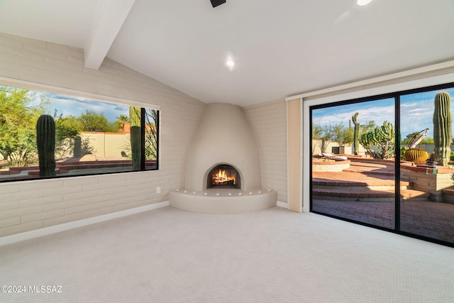 unfurnished living room featuring brick wall, a large fireplace, lofted ceiling with beams, and carpet flooring