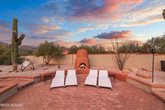 patio terrace at dusk featuring exterior fireplace and a mountain view