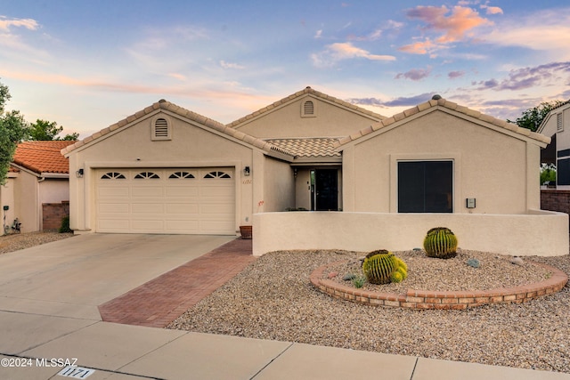 ranch-style home featuring driveway, a tiled roof, an attached garage, and stucco siding