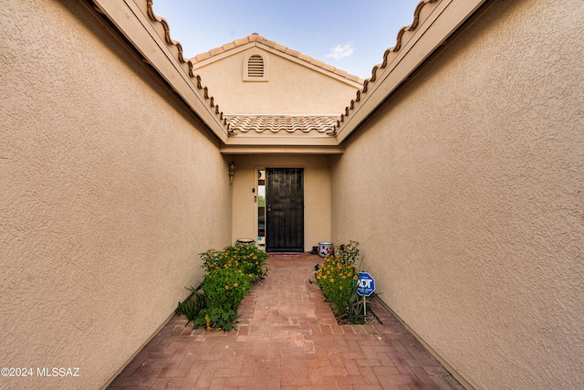 view of exterior entry with a patio area, a tile roof, and stucco siding