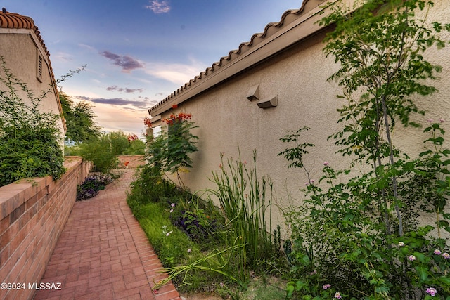 view of side of home with fence, a tiled roof, and stucco siding