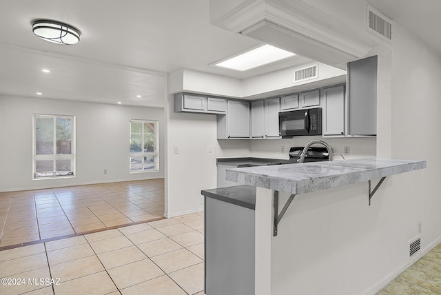 kitchen featuring gray cabinetry, light tile patterned floors, a kitchen breakfast bar, and kitchen peninsula